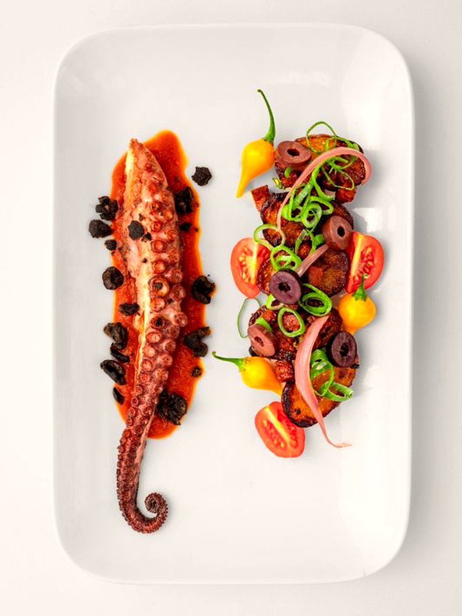 Poulpe grillé et condiments colorés sur plat rectangulaire